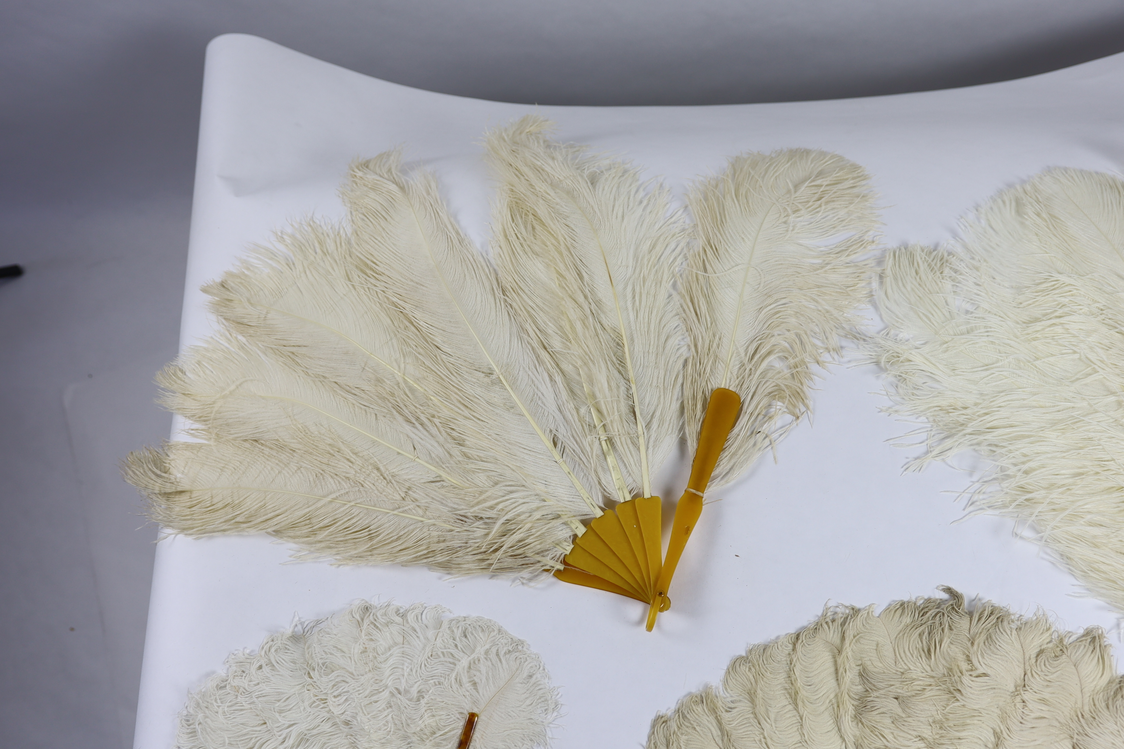 Two early 20th century Ostrich feather and mother of pearl fans, another similar fan with amber Bakelite handle and a small tortoiseshell and feather fan (4)